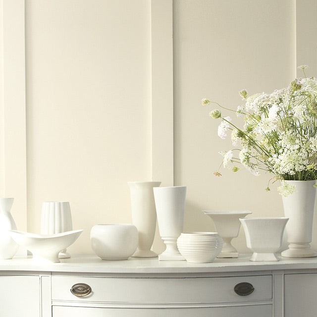 A warm white painted wall creates a soft backdrop for vases and flowers atop a traditional console.
