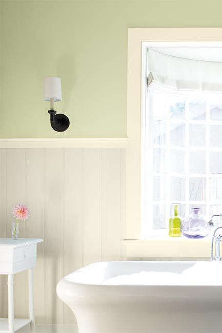 A light green-painted bathroom, detailed with white wainscoting and a stand alone tub.