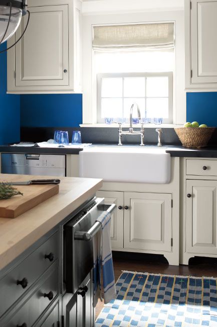 A blue-painted kitchen with white cabinets, a butcher block countertop island and white farmhouse sink.