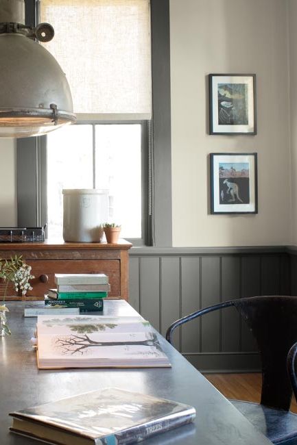 A gray painted room with gray trim and wainscoting, accented by an eclectic light, and long black modern table.