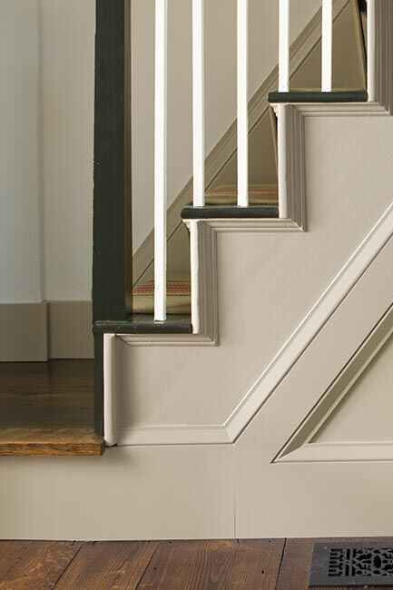 A sideview of white-painted stairs with white spindles and black handrail.