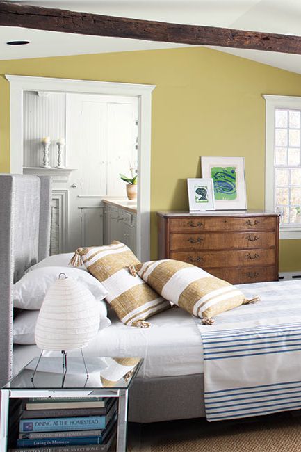 Exposed ceiling beams and yellow walls painted with Anjou Pear AF-425 creates a cozy bedroom.