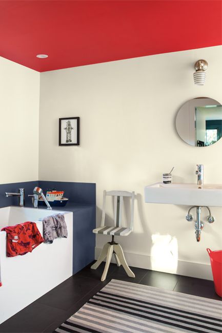 A bathroom features a round mirror over a contemporary sink; black and white colored walls and floors are accented by a red ceiling.