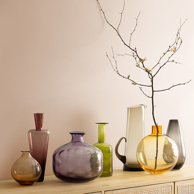 Dusty pink walls behind a rattan cabinet with an array of glass vases placed on top.