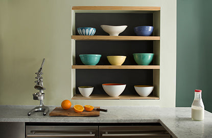 Monochromatic kitchen walls with shades of dark and light green including three inset shelves holding 9 bowls.