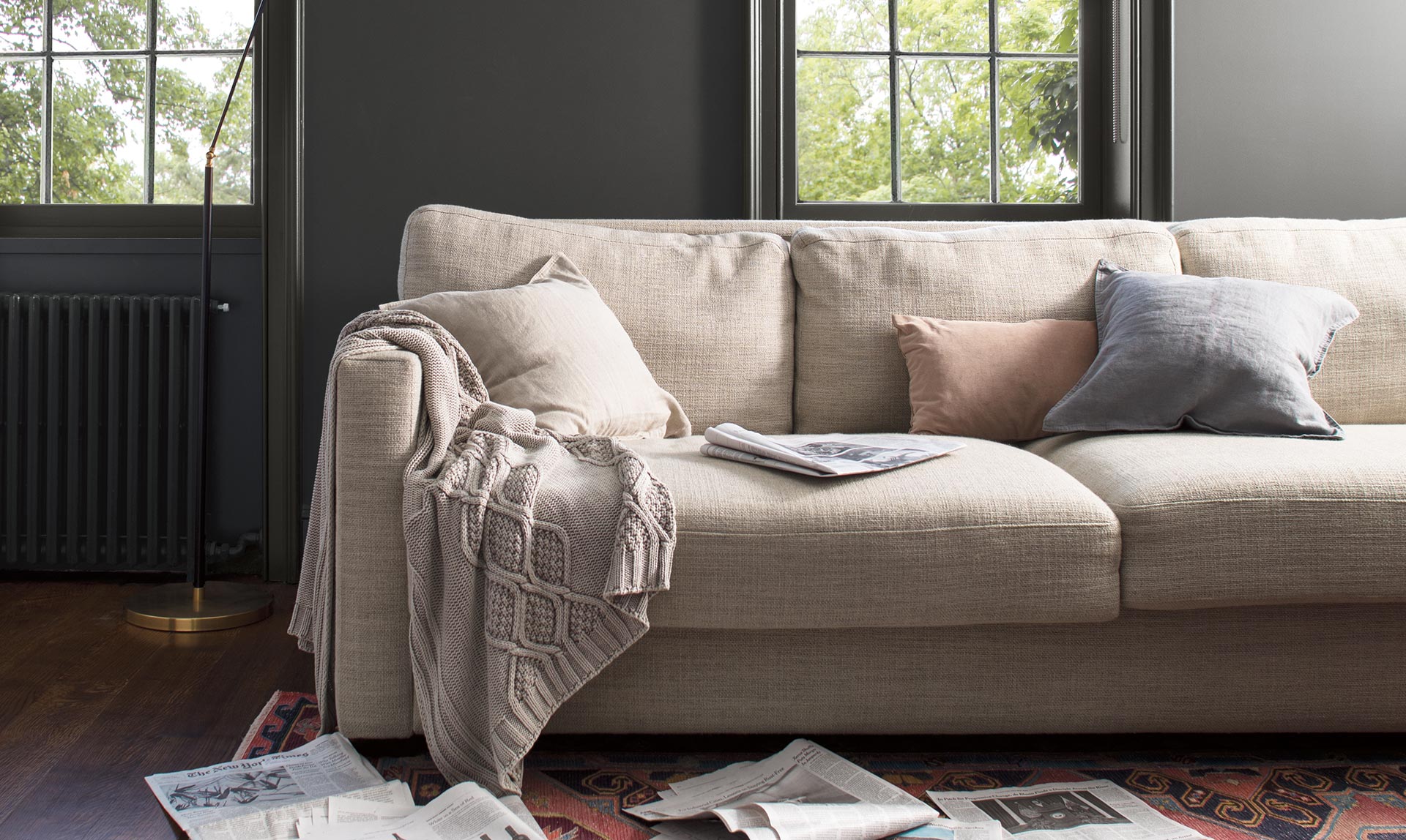 Charcoal gray-painted walls, trim and windows add depth to a cozy family room with beige couch. Color of the Year 2019