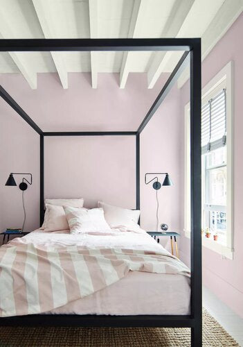 New Age purple-painted bedroom with black bedframe, White Heron-painted ceiling and trim, striped pink bedspread, and black wall lamps.