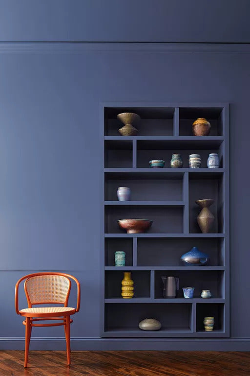 A serene space with built-in shelving and wall all painted in a deep blue with a small leather club chair.