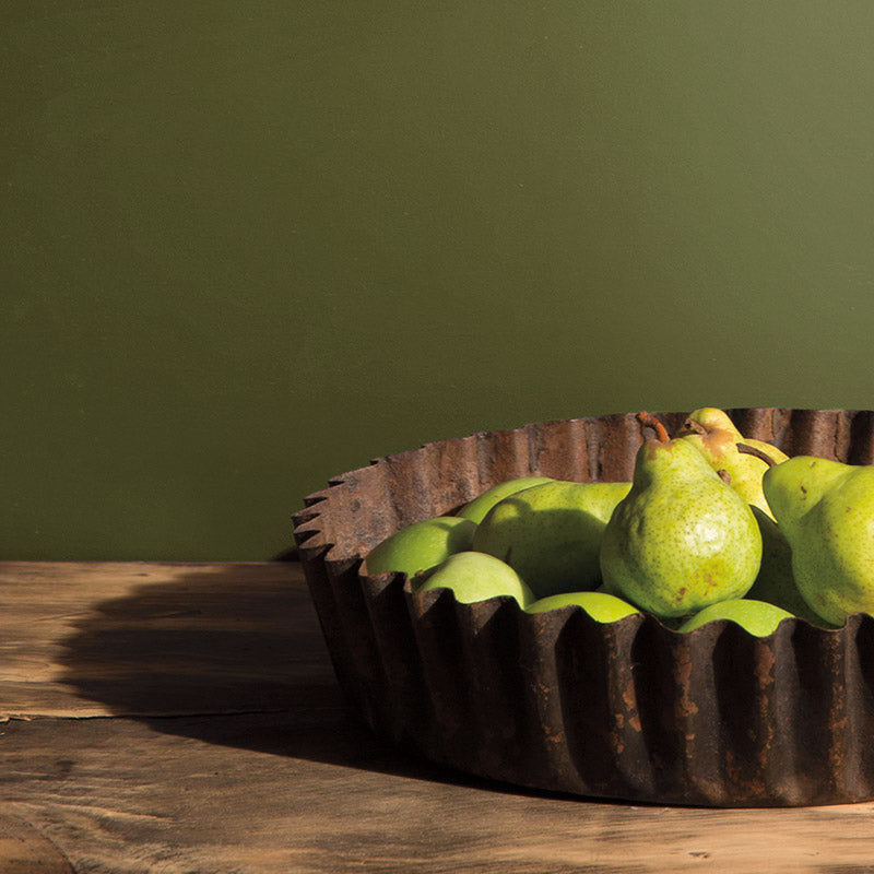 Bowl of pears on a rustic wooden table with olive green wall.