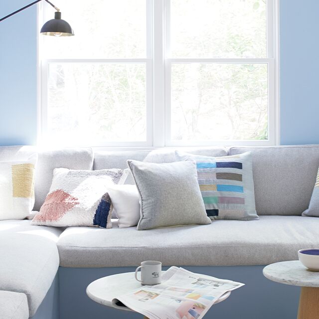 A living room with two blue walls and one white shiplap wall, featuring a large, gray sectional couch and three small end tables.