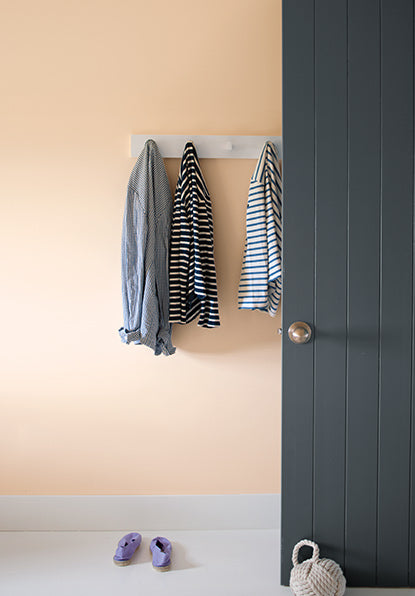 A peach-painted wall with white trim and gray doors, featuring a set of white coat hooks with various shirts.
