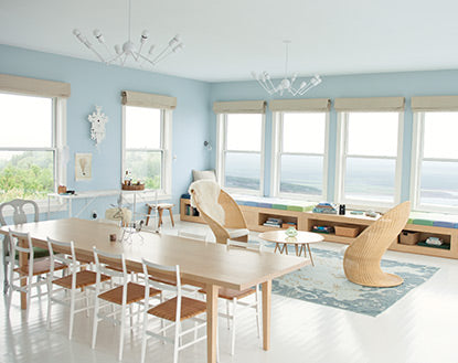 A blond wood dining table underneath two modern chandeliers besides an airy seating area features a wall of windows boasting sweeping Nova Scotia views.