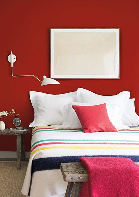 Bedroom with red-painted walls, white trim, black bookcase, colorful bedding, and wooden accent tables.