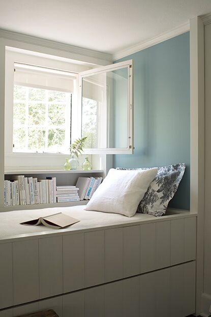 White room with blue-painted accent wall behind a built-in reading nook with an open window.