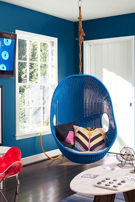Game room with blue-painted walls, white ceiling and trim, blue hanging chair, red accent chair, and various décor.