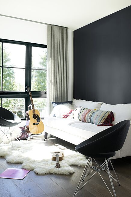Living room with white walls and ceiling, black accent wall, white sofa, black accent chair, guitar, and white faux-fur rug.