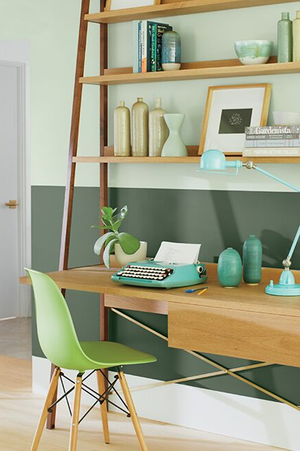 Wooden desk and green chair in front of a two-toned green wall.