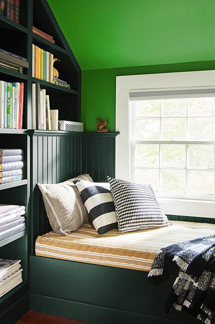 Bedroom with bookshelf and bed frame in dark green, mid-toned green ceiling, and window with white trim.