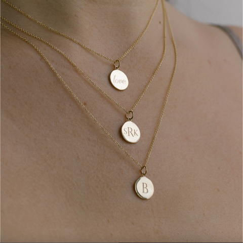 Woman wearing layered necklaces with engraved round charms