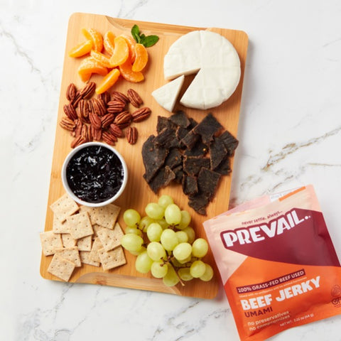 A tray filled with various fruits, crackers and beef jerky