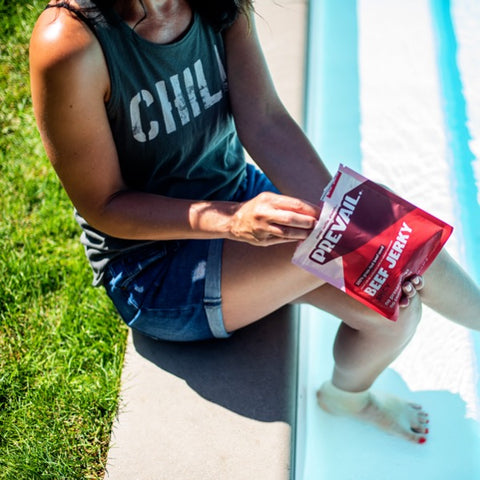 Woman sitting next to a pool while snacking on PREVAIL beef jerky