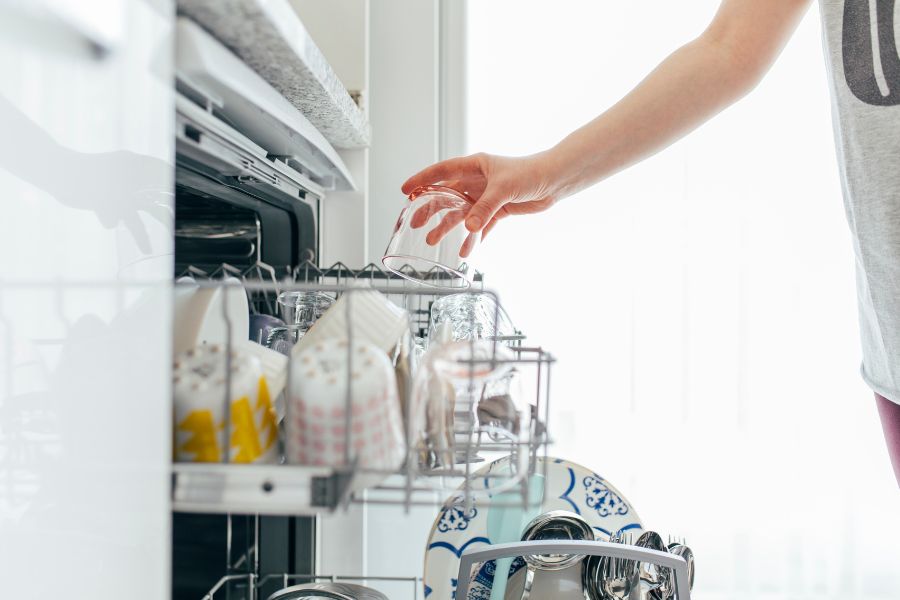 Open dishwasher with woman loading glass cup