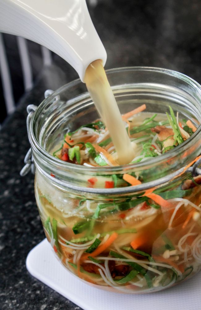 Hot water being poured into a jar with noodles and vegetables