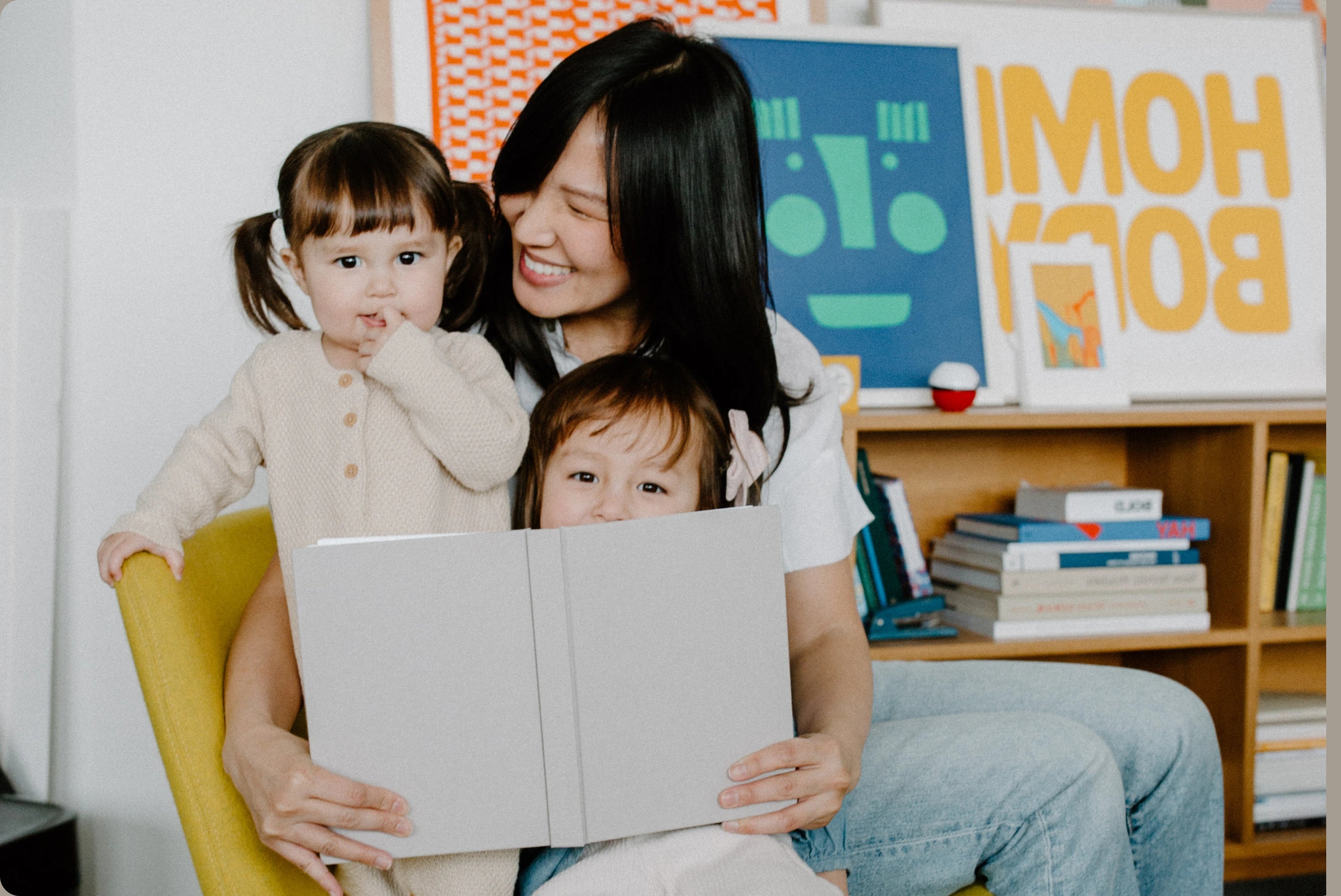 A mother reads a book with her two young children in a cozy room.