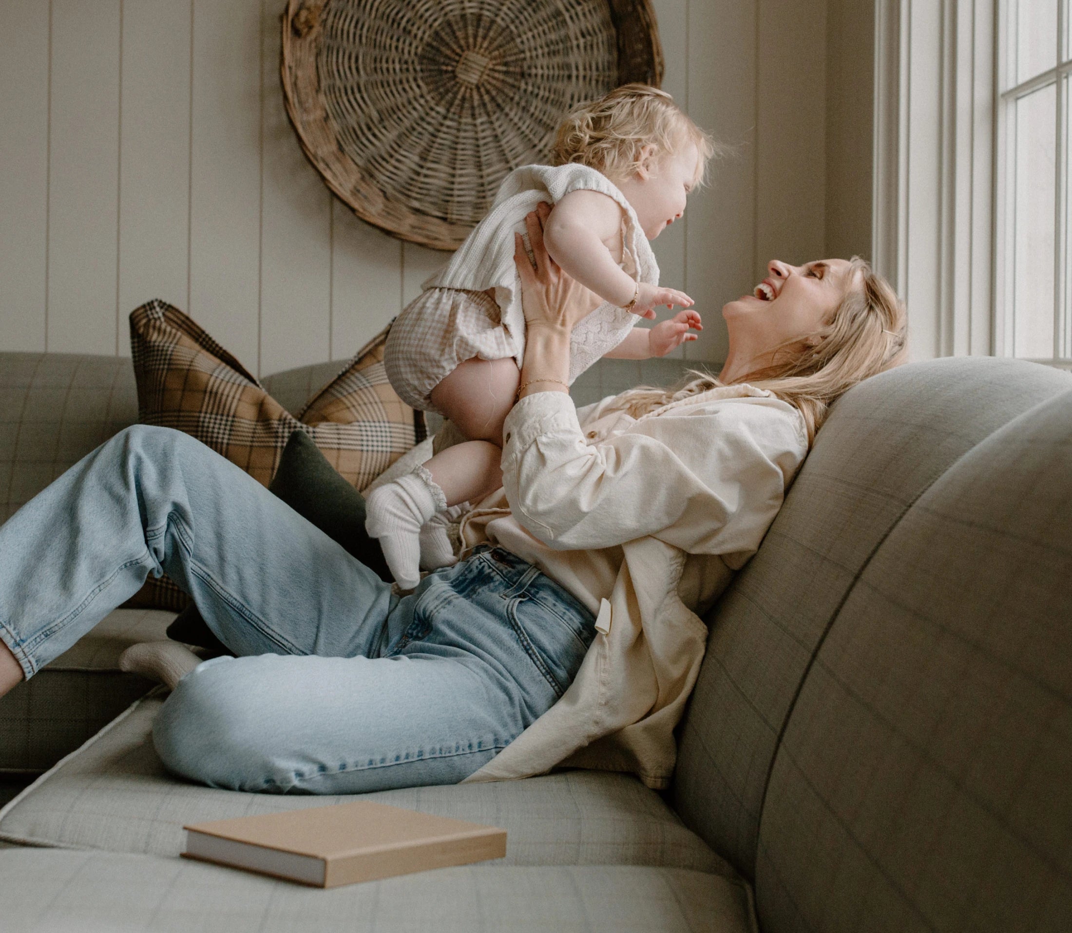 A woman joyfully holding up a baby on a cozy couch.