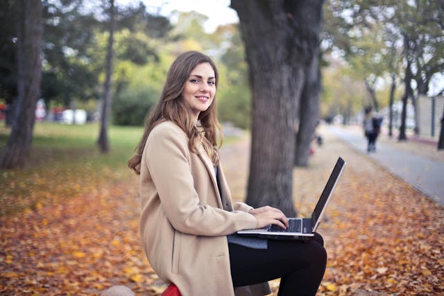woman siting on a park bench with a computer writing a resume