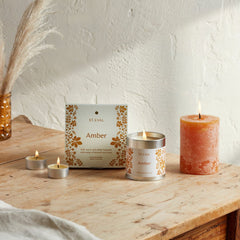 Lit Amber candle collection with orange pillar and packaging on a wooden table