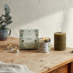 Lit Moss candle collection with green pillar and packaging on a wooden table