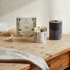 Lit Oak candle collection with dark brown pillar and packaging on a wooden table
