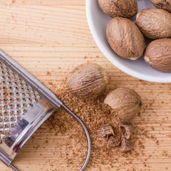 Whole roasted nutmeg seeds with a silver grater dusted with ground nutmeg