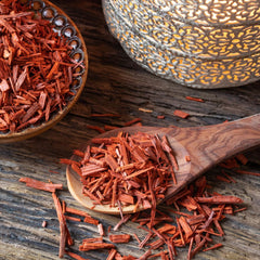 Reddened sandalwood chips in a bowl and sprinked over a wooden tabletop