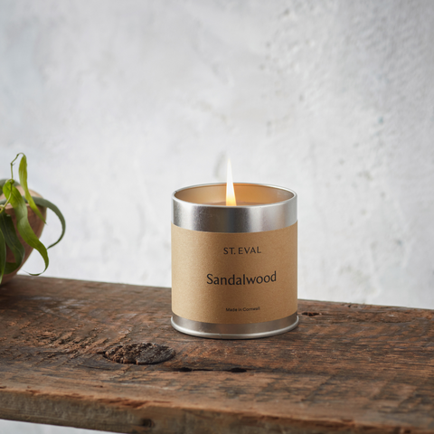 Sandalwood Scented Tin Candle on wooden shelf with a plant in the background