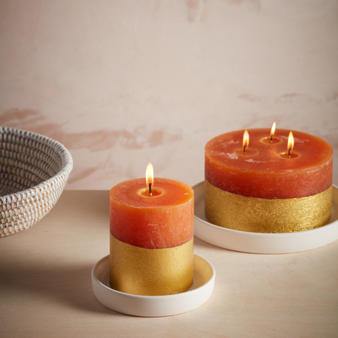 Lit Orange and Cinnamon Gold Half-Dipped Pillar and Multiwick candle on white ceramic plates