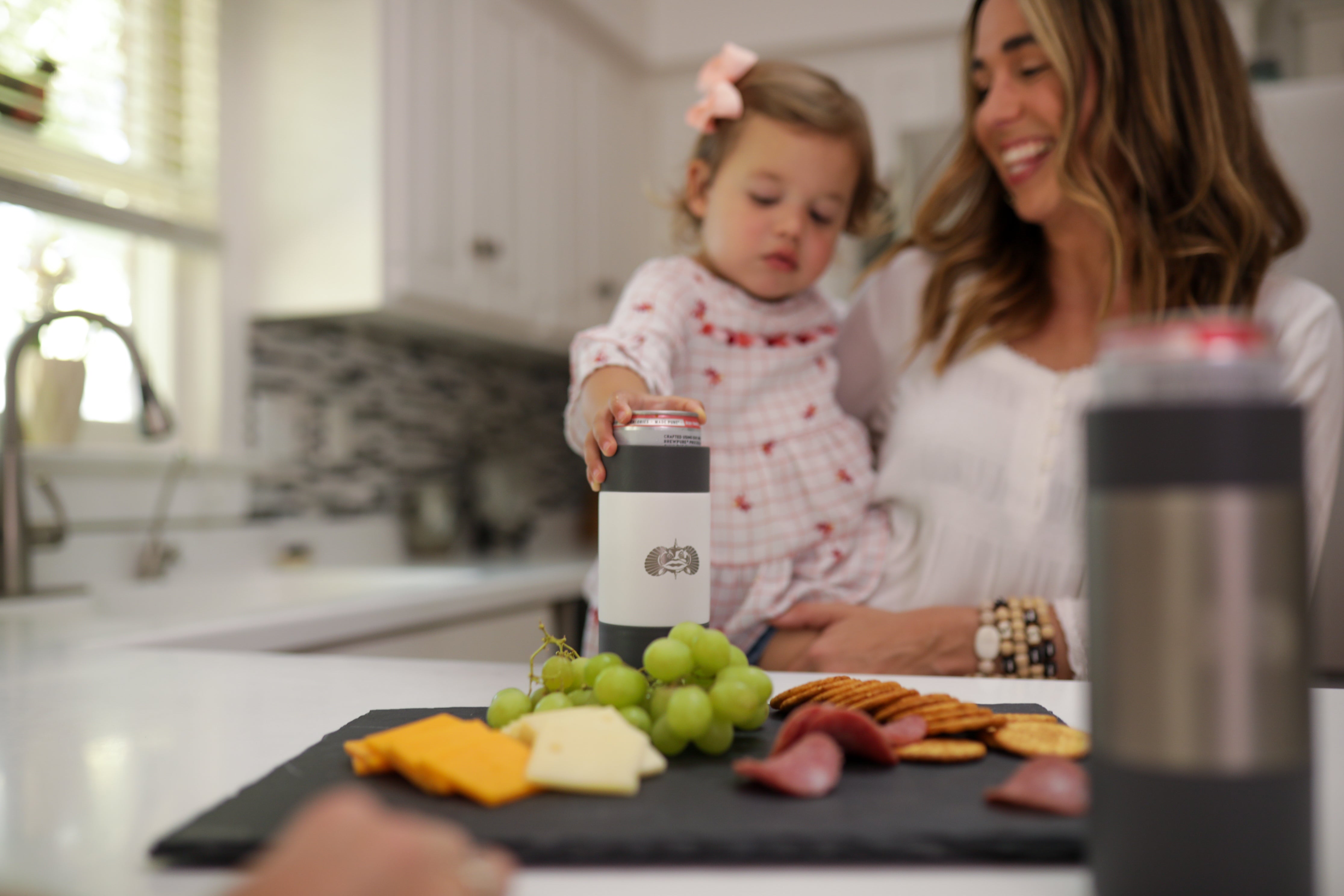 Mother's day, mom holding a baby while baby grabs for cup on countertop with food on it