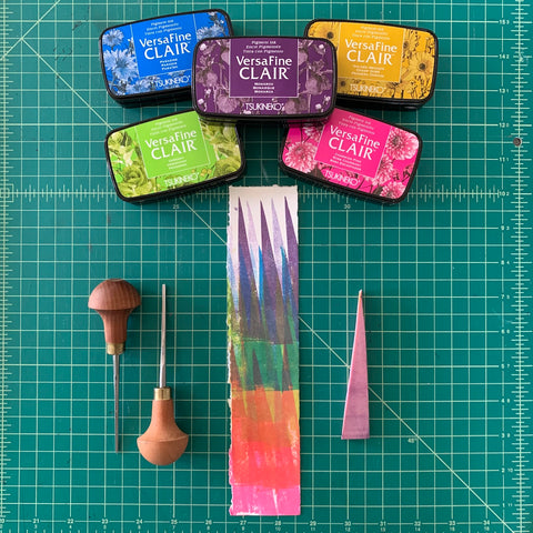 A colorful long and narrow print of colorful block printed triangles accompanied by colorful stamp pads and carving tools.