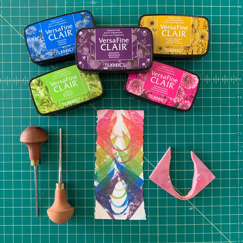 A colorful block print of curved shapes accompanied by colorful stamp pads and carving tools.