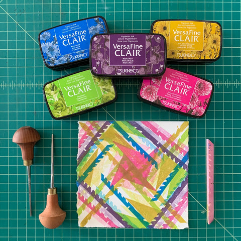 A flatlay of a multicolored square print, accompanied by colored stamp pads and carving tools.