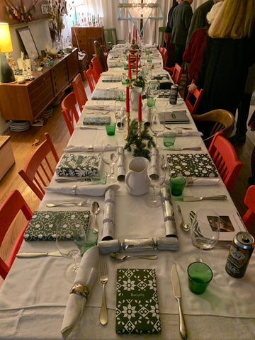 A long Christmas Table ornately and colorfully set with people gathered in the background
