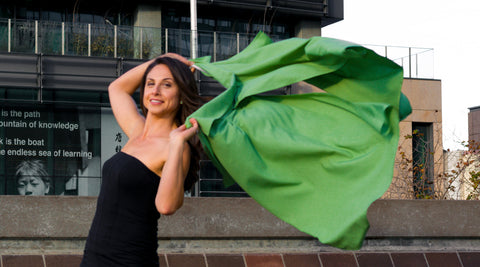 Model holding UV sun protection sol Escape in apple green with wind unfurling the cape behind her.