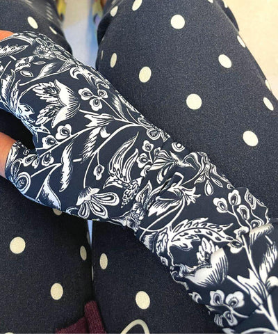 Heliades Sun Protective Clothing UV Arm Sleeves in navy blue and white floral print and made of UPF 50 patterned fabric. Arm rests on polka dot pant leg.