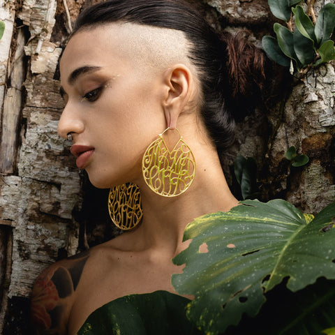 Alternative model wears large gold hoop earrings that say 'Mamacita' in an italic font