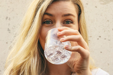 Blonde Frau trinkt aus Wasserglas
