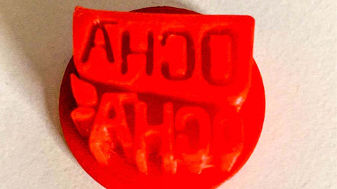 Ocha-Ocha® Stempel aus dem 3D-Drucker. Er ist knallrot und zeigt das Logo scheinbar spiegelverkehrt.