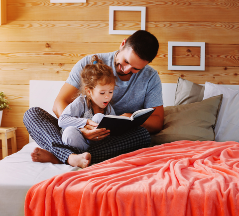 Dad reading to his daughter before bed on bed with Bedsure fleece blanket