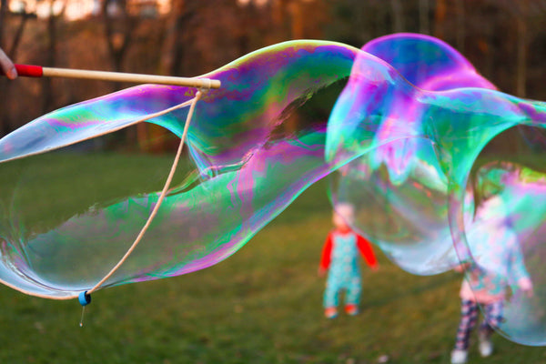 Dr Zigs Giant Bubbles creating a rainbow of colours with 2 children in the background out of focus