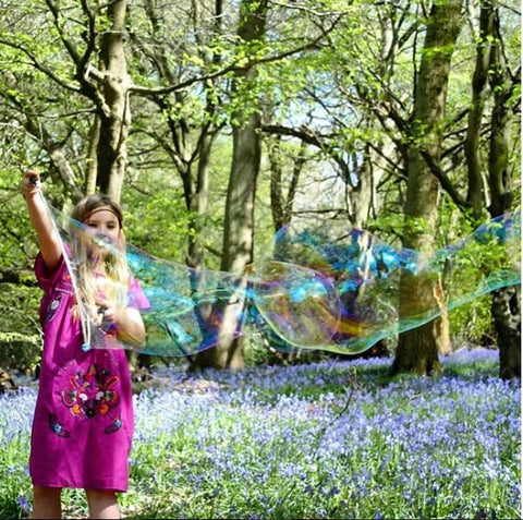 Girl playing with Dr Zigs Bubbles in a field of bluebells.  Wooden toys are best for kids, and with multicoloured bubbles even more so.  